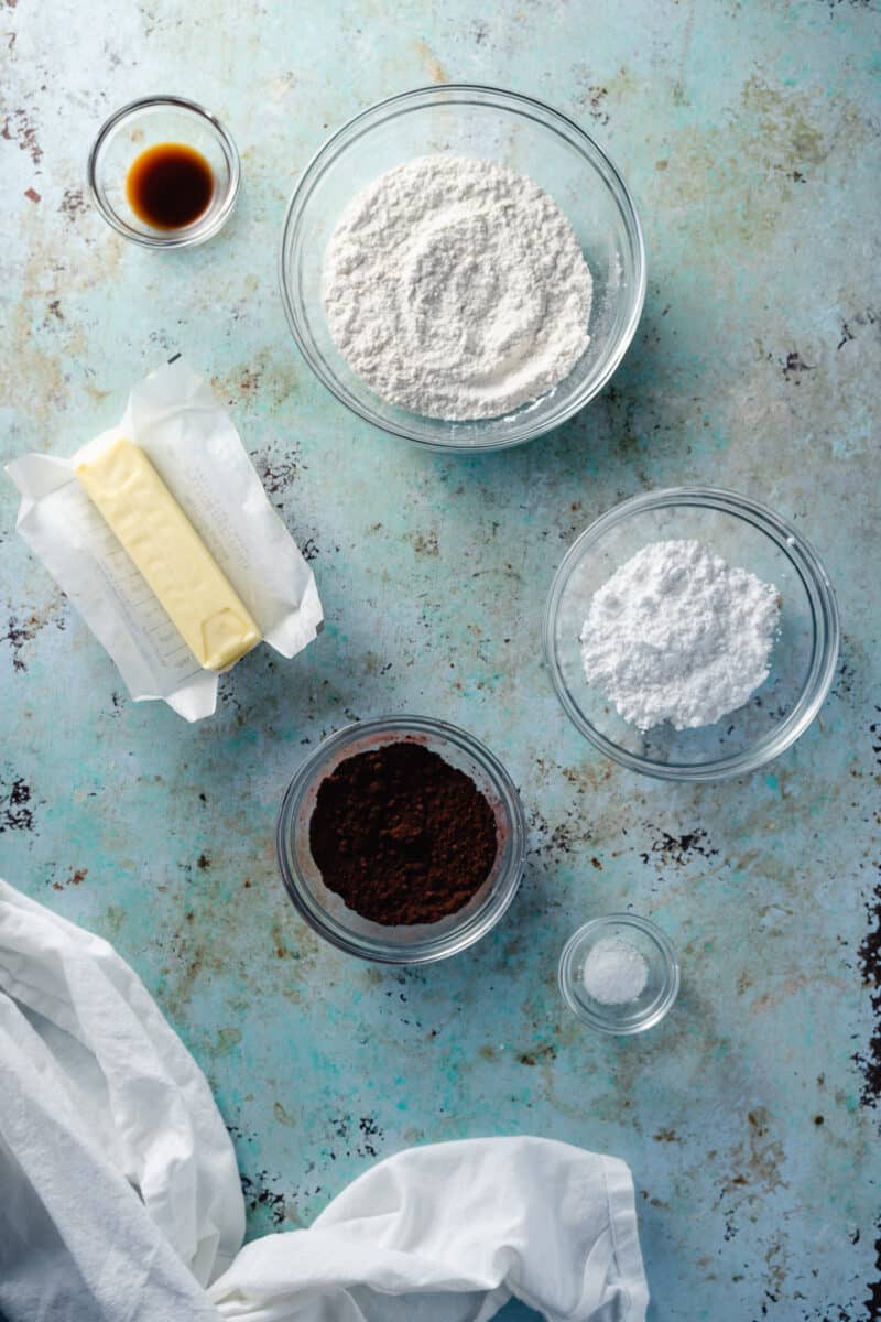 Bowls of flour, powdered sugar, cocoa powder, vanilla extract, and a stick of butter