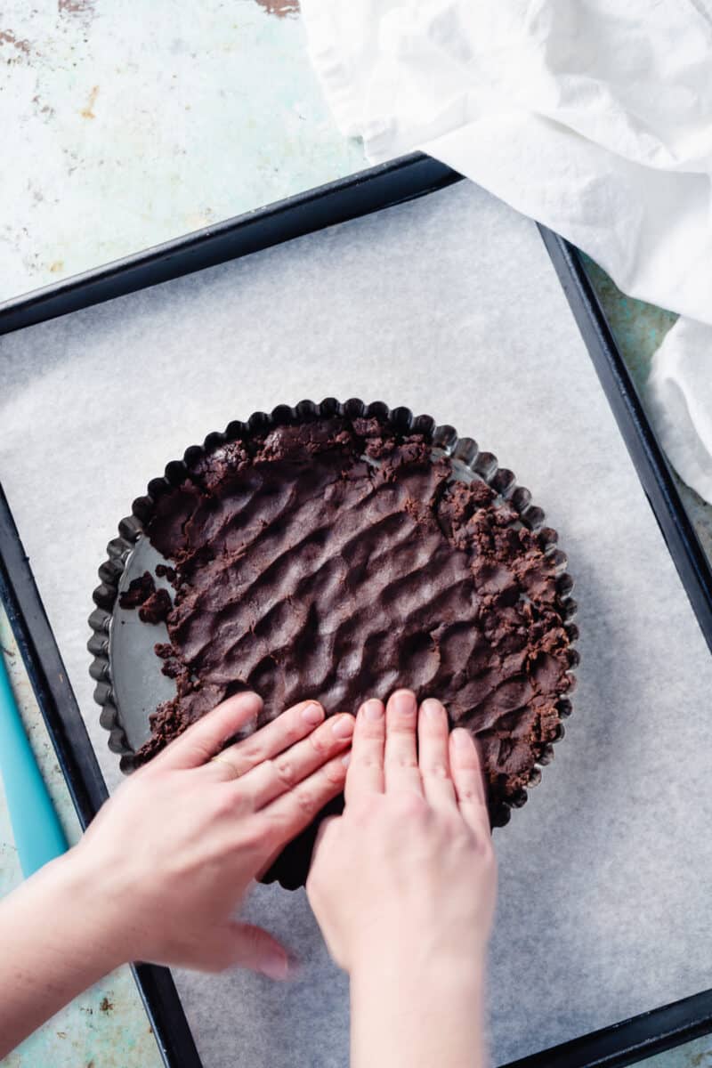 Hands pressing the chocolate tart dough into the tart pan