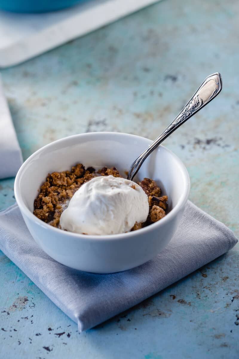 Apple Crisp in a white bowl with a scoop of vanilla ice cream and a spoon