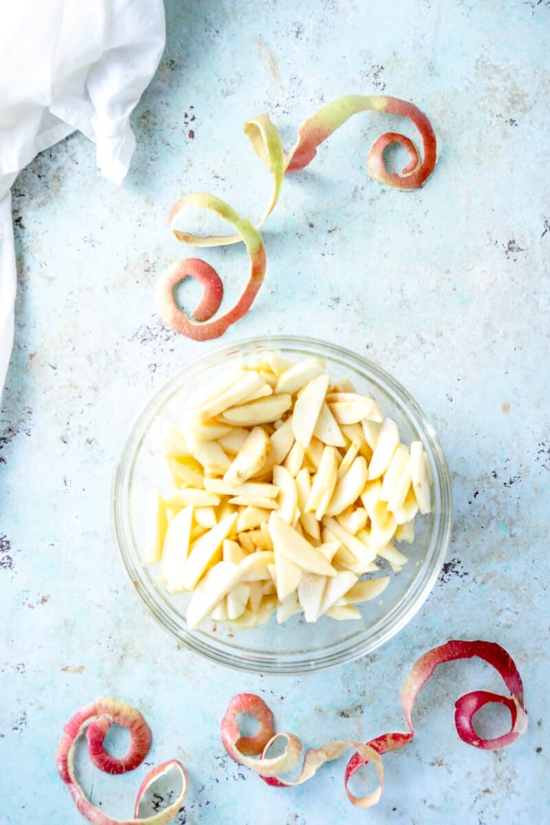 Sliced apples in a bowl with apple peels on the counter