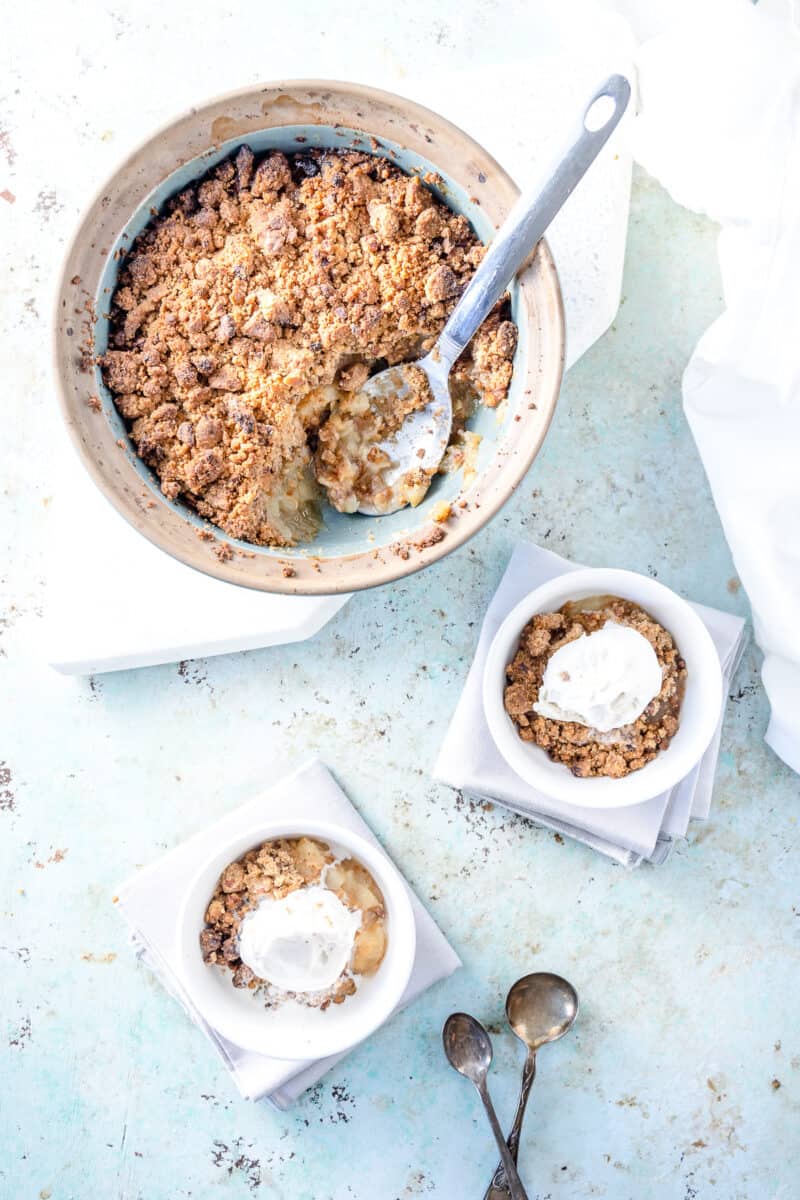 Apple crisp in a baking dish with bowls of crisp topped with ice cream and spoons nearby