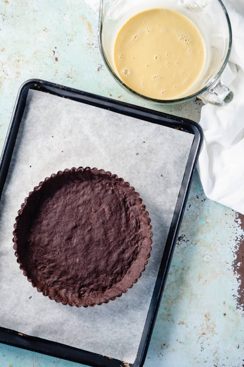 Chocolate shortbread tart crust on a baking sheet with filling next to it