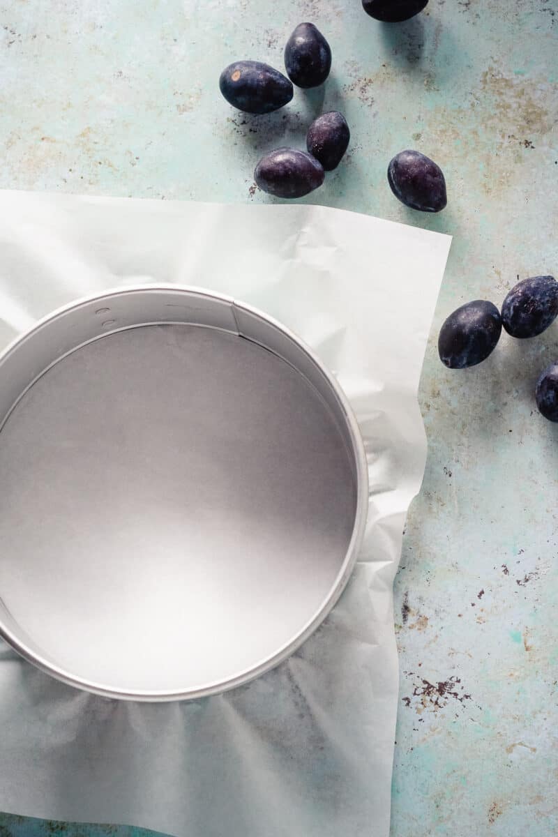 Cake pan lined with parchment paper and plums nearby