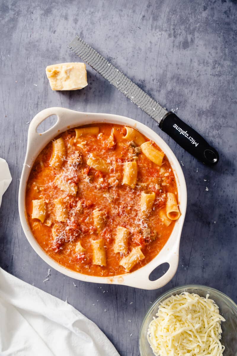 Ziti in tomato sauce with a block of parmesan cheese and mozzarella nearby