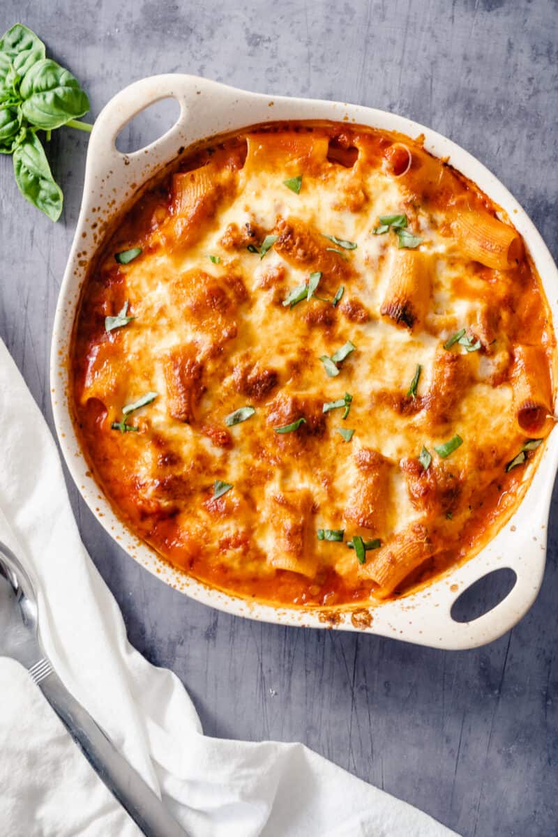 Baked Ziti in an off-white baking dish with basil on the side