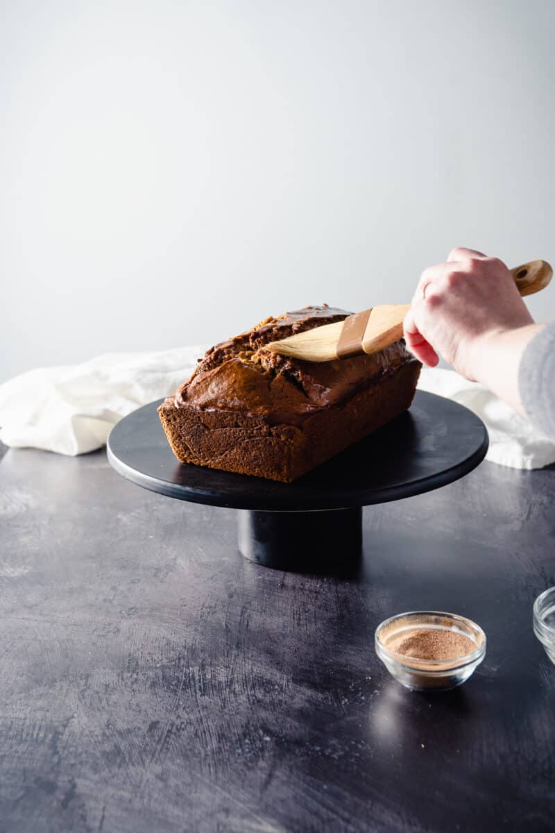 Hand brushing melted butter over the top of a warm loaf of pumpkin bread