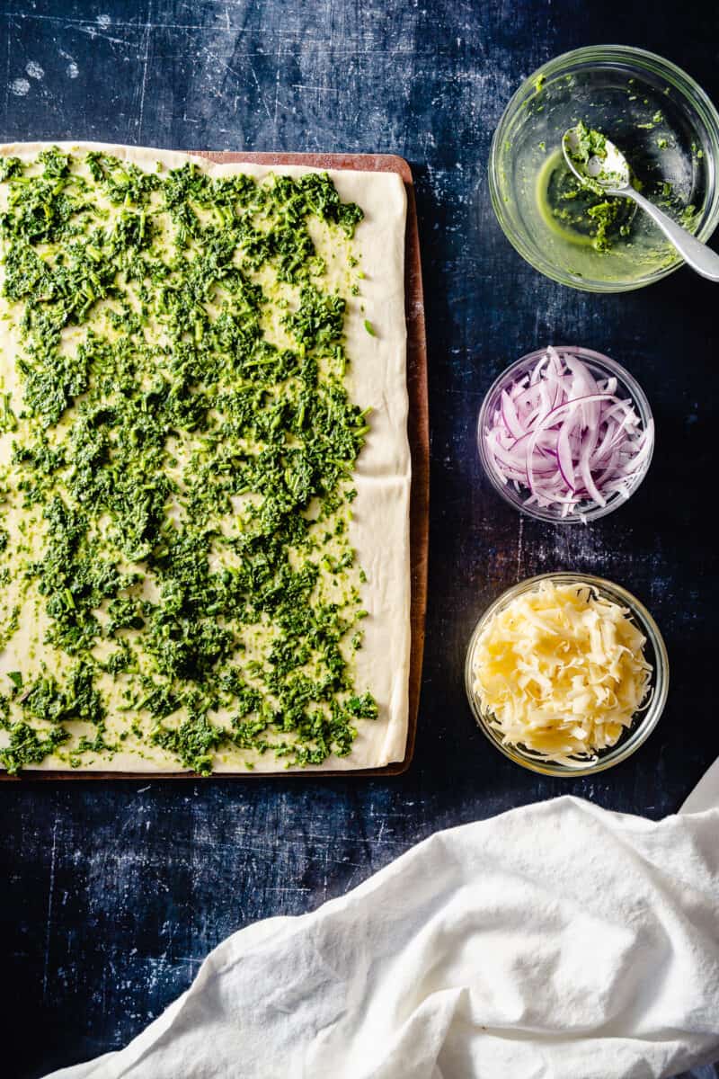 Puff pastry spread with green chutney, with red onion and cheddar cheese in bowls