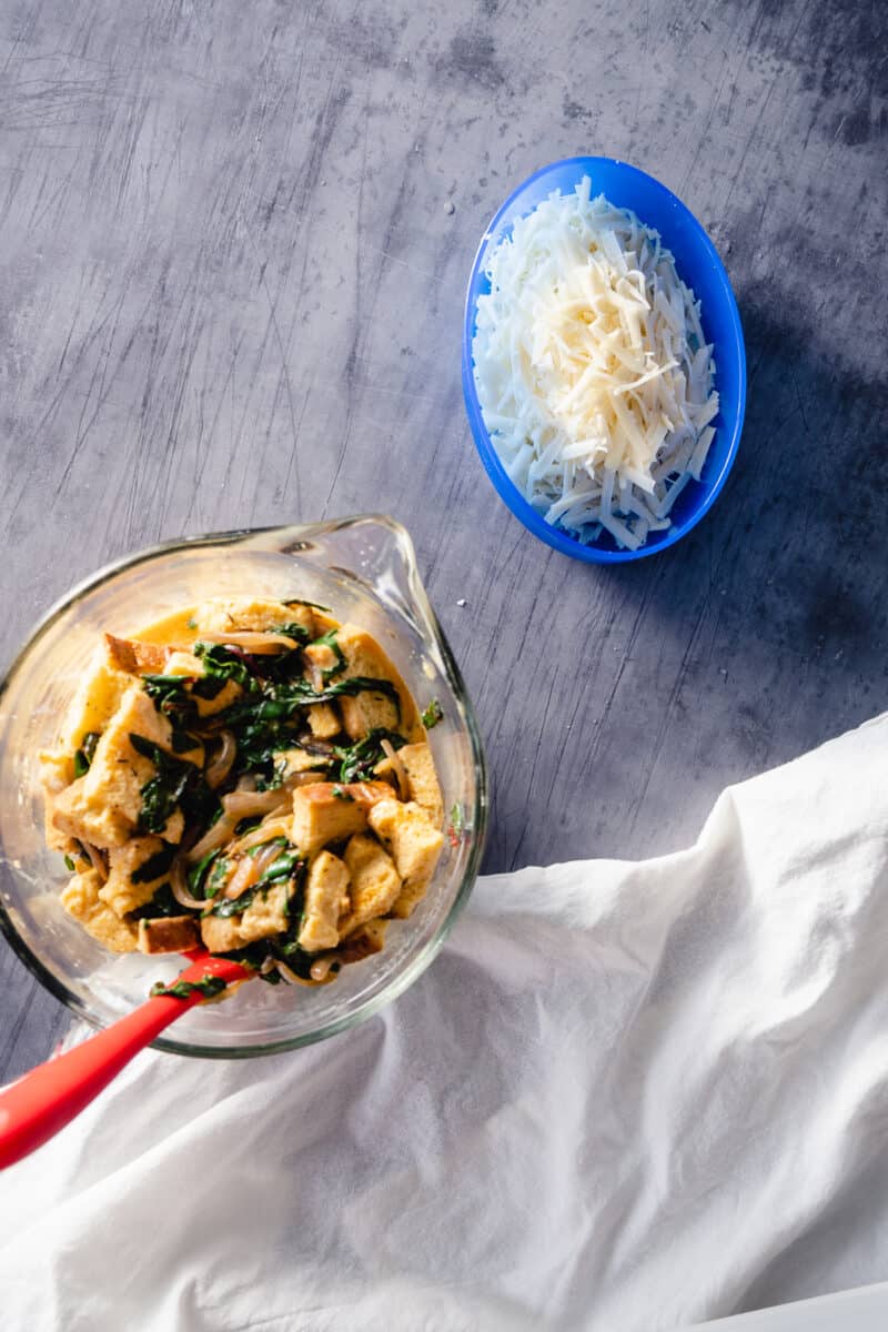 Bread cubes and chard in a custard mixture with grated cheese in a separate bowl