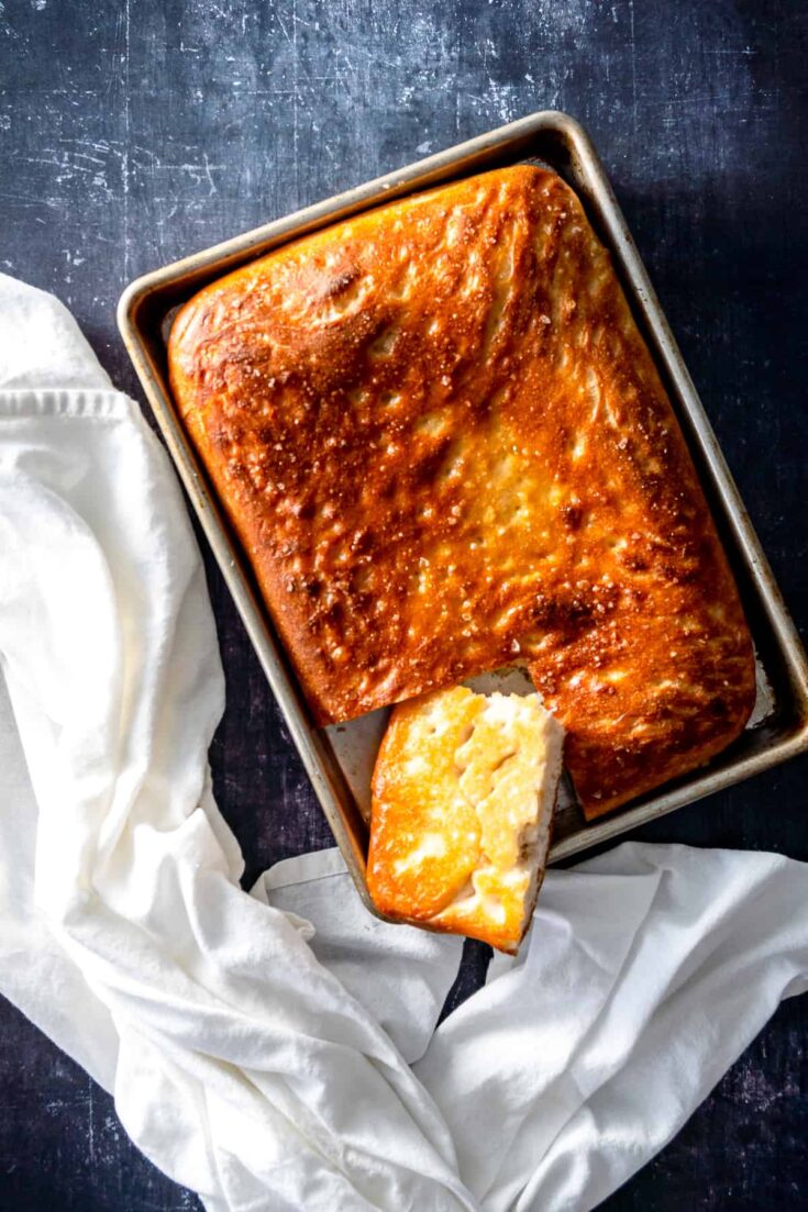 Focaccia in a sheet pan with a piece cut out showing the crisp bottom