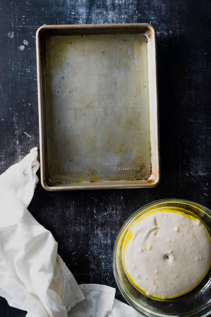 Doubled focaccia dough in a bowl next to an oiled pan