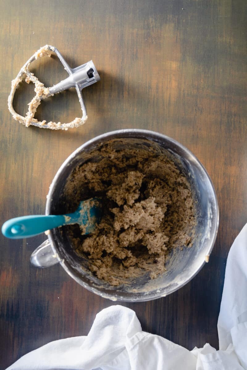 Mexican wedding cookie dough in a stand mixer bowl with a paddle coated in dough alongside