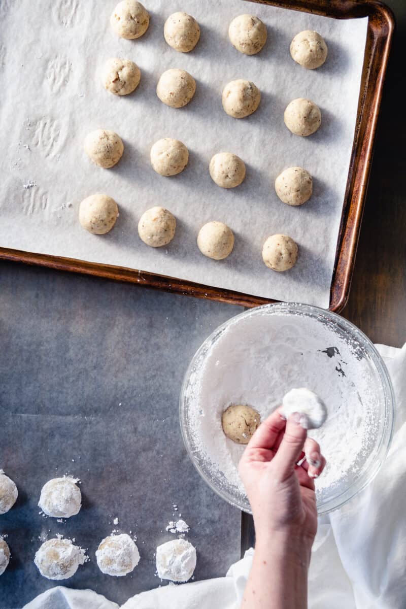 Mexican wedding cookies getting rolled in powdered sugar