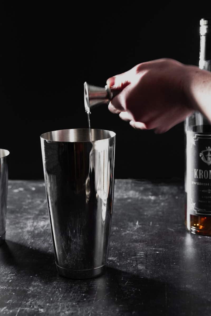 Hand pouring rum into a cocktail mixing tin