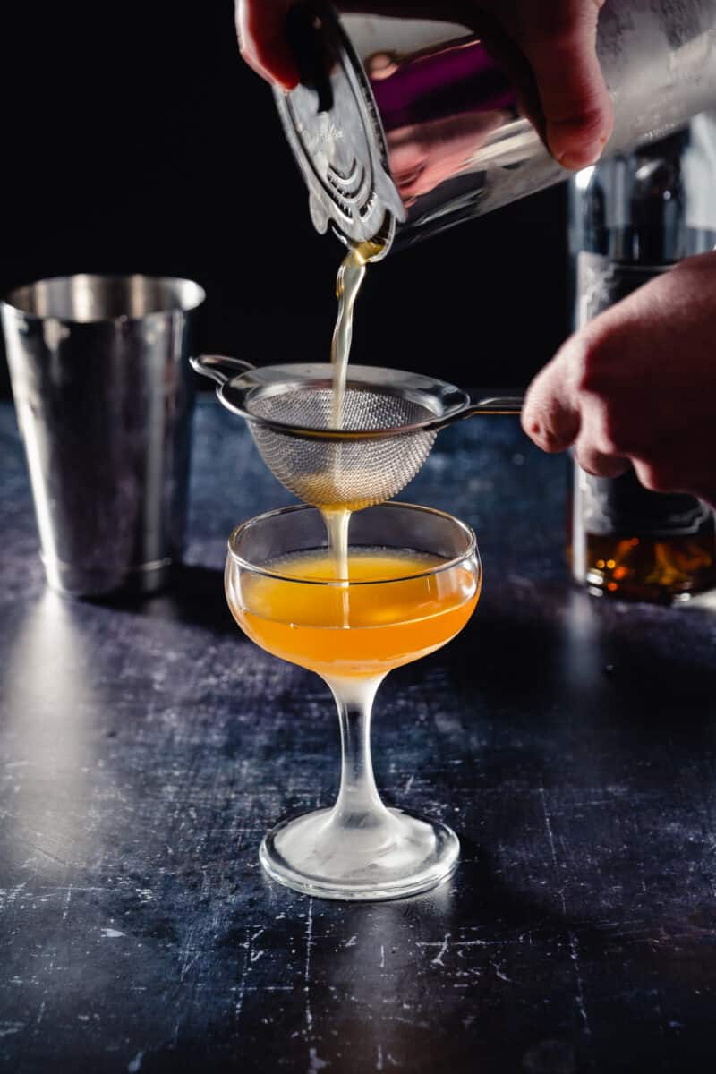 Double-straining the Doctor cocktail through a Hawthorne strainer and a mesh strainer