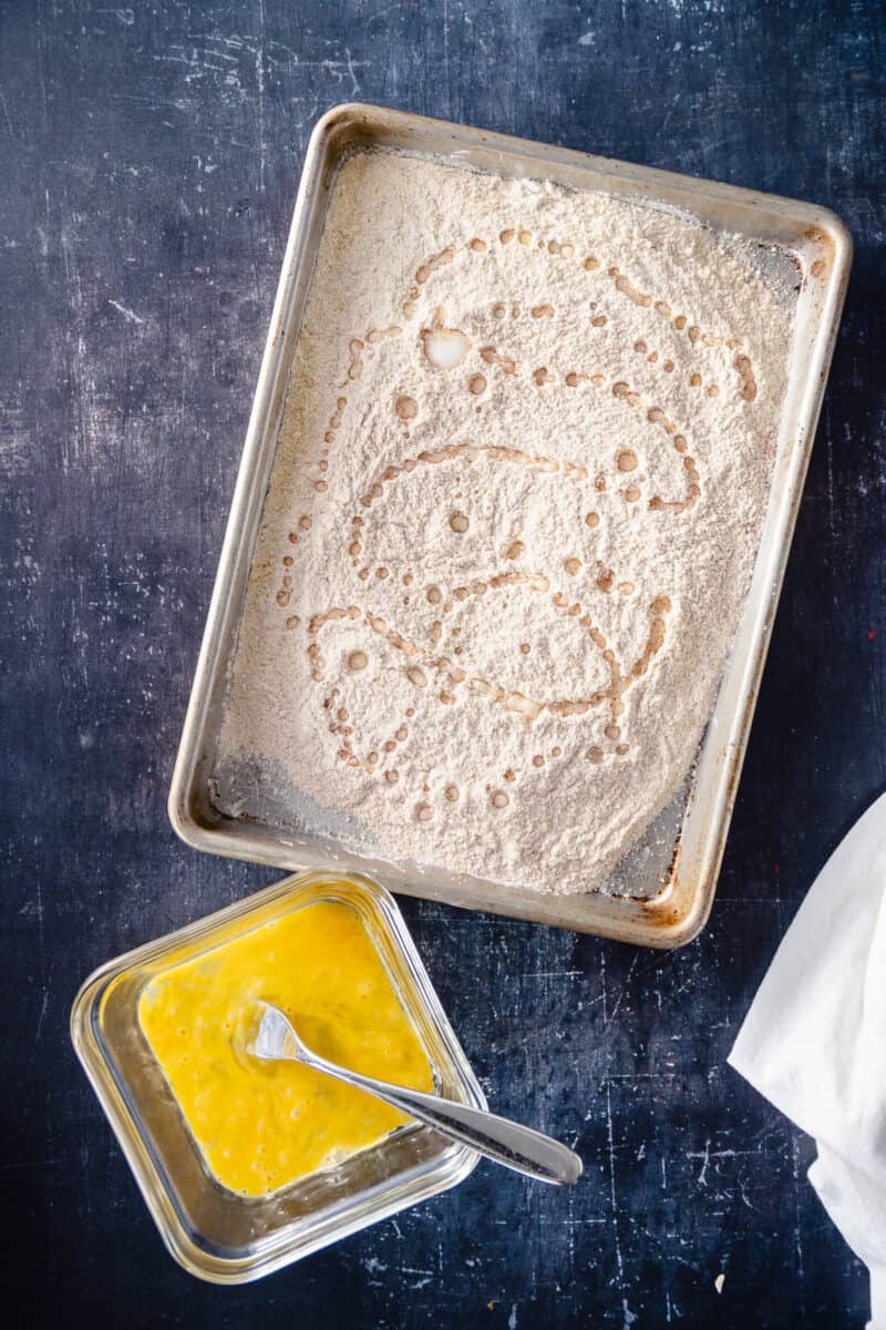 Flour and cornmeal breading mixture with a dish of whisked egg nearby