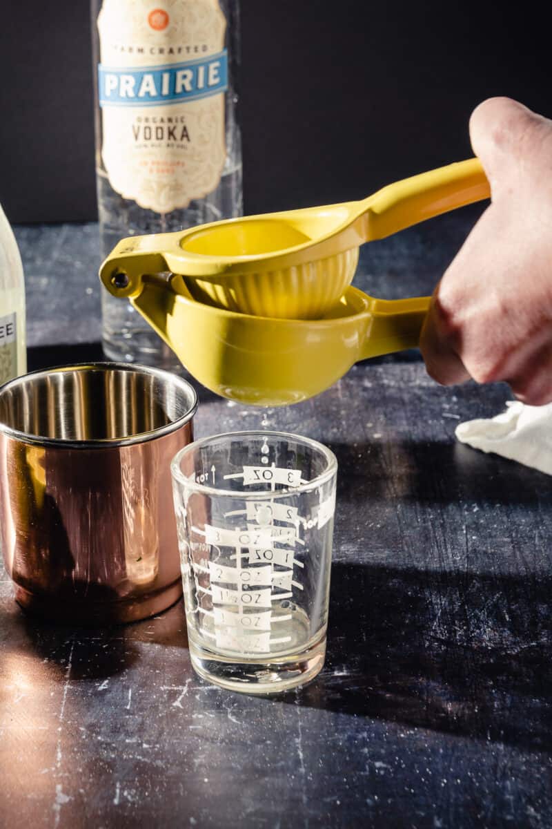 A yellow citrus squeezer juicing a lime into a glass