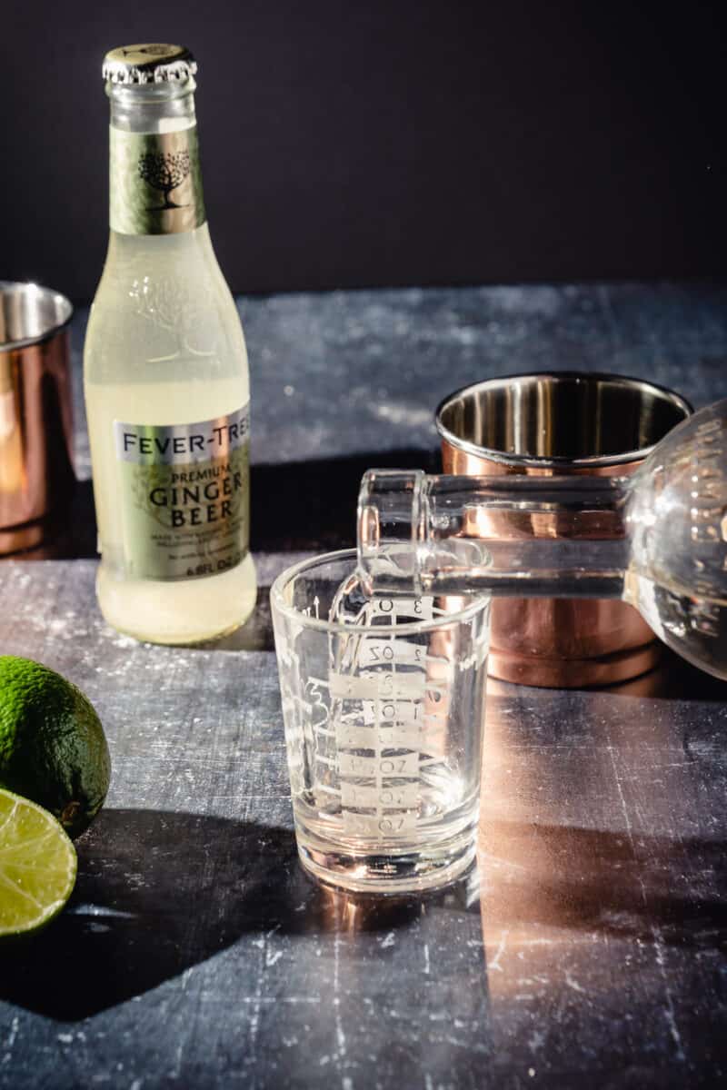 Vodka being poured into a measuring glass with a copper cup behind