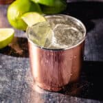 Moscow Mule cocktail in a copper tumbler with limes in the background