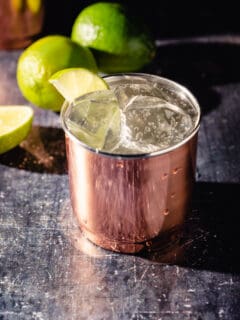 Moscow Mule cocktail in a copper tumbler with limes in the background