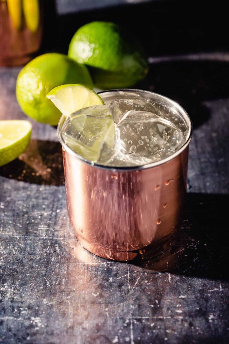 Moscow Mule cocktail in a copper tumbler with limes in the background