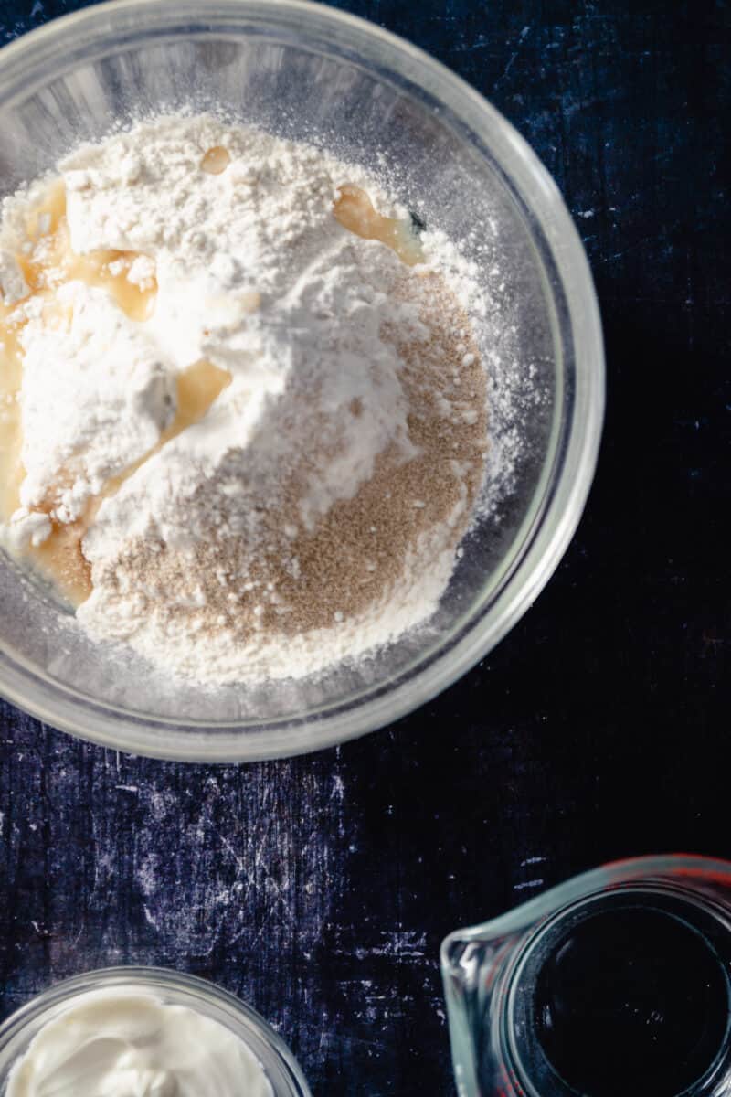 A mix of flour, oil, yeast, baking powder, and salt in a clear glass mixing bowl