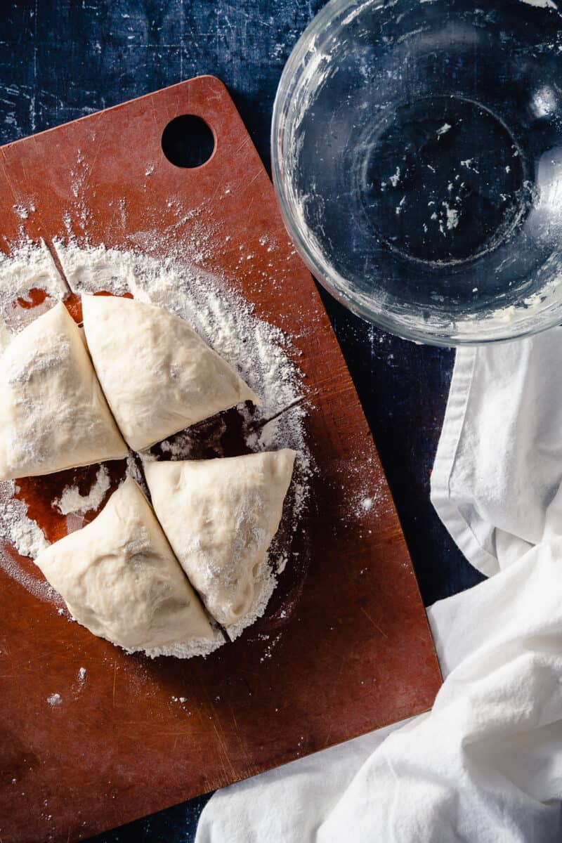 Naan dough divided into 4 pieces on a flour-dusted cutting board