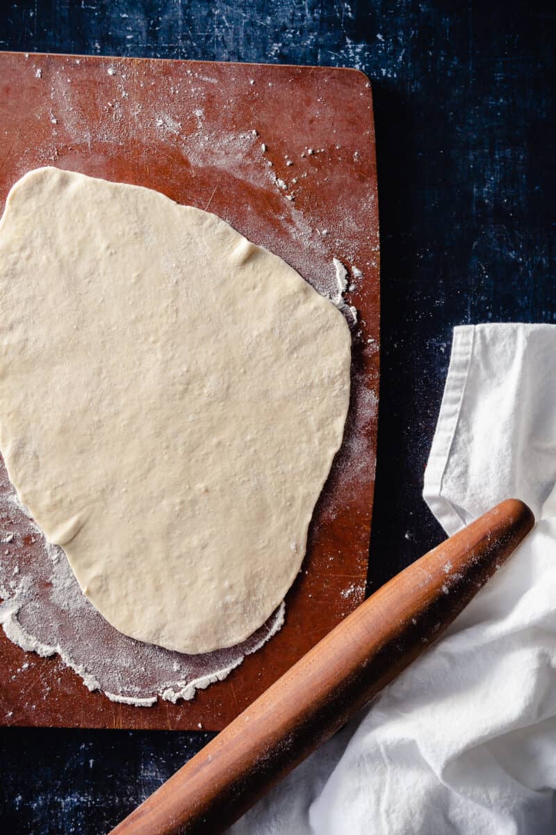 Naan dough rolled out on a flour-dusted cutting board with a rolling pin