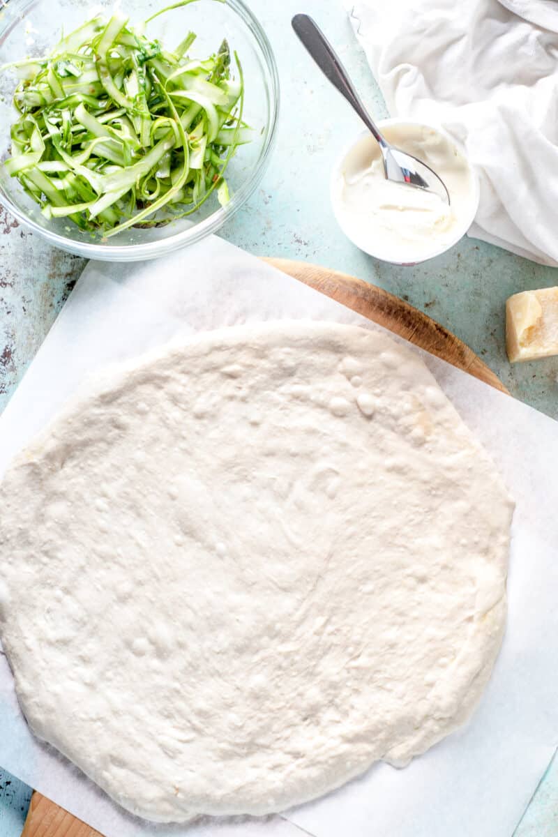 Shaved asparagus in a bowl, creme fraiche, pizza dough on parchment paper