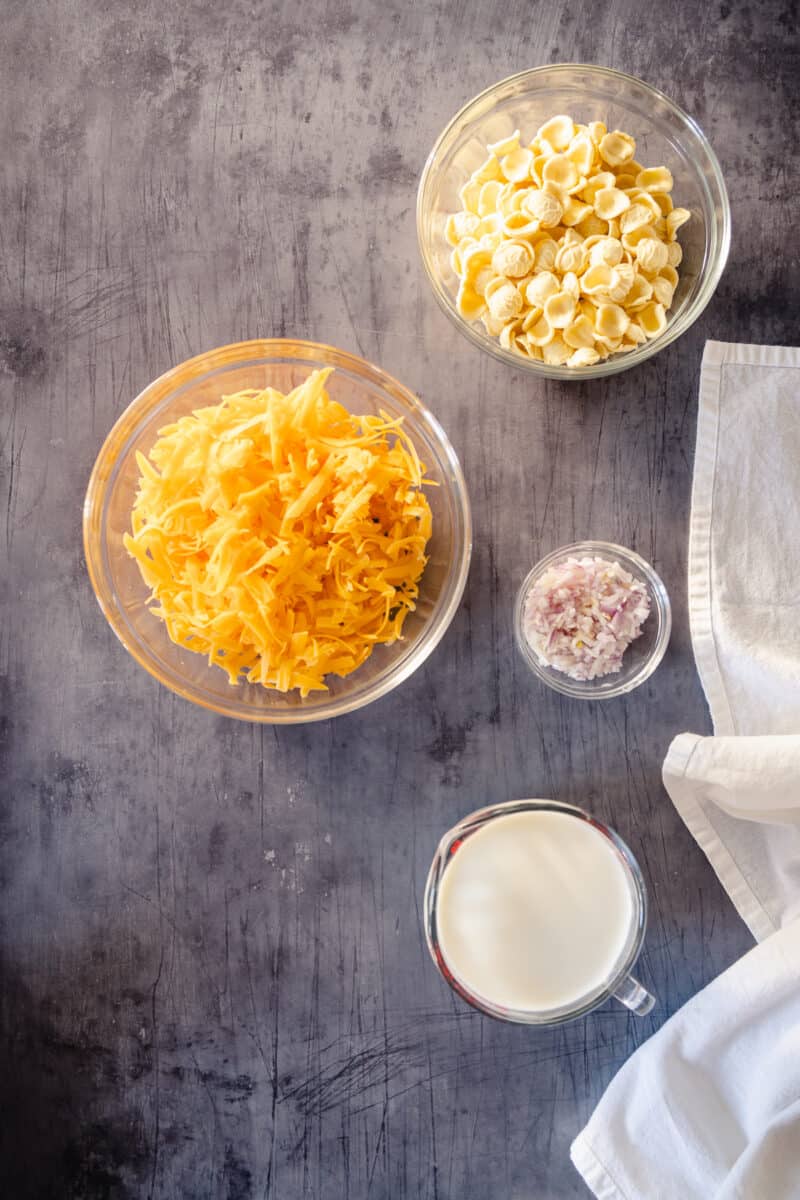 Orrecchiette, shredded cheddar cheese, minced shallots in glass bowls and milk in a measuring cup