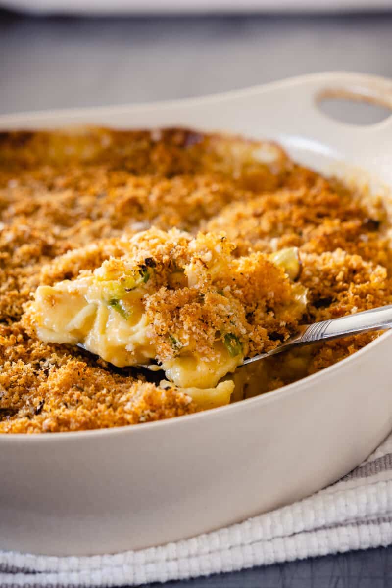 A serving spoon lifting out some Brussels sprouts mac and cheese from a casserole dish, close up