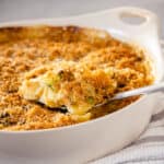 A serving spoon lifting out some Brussels sprouts mac and cheese from a casserole dish