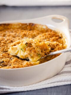 A serving spoon lifting out some Brussels sprouts mac and cheese from a casserole dish