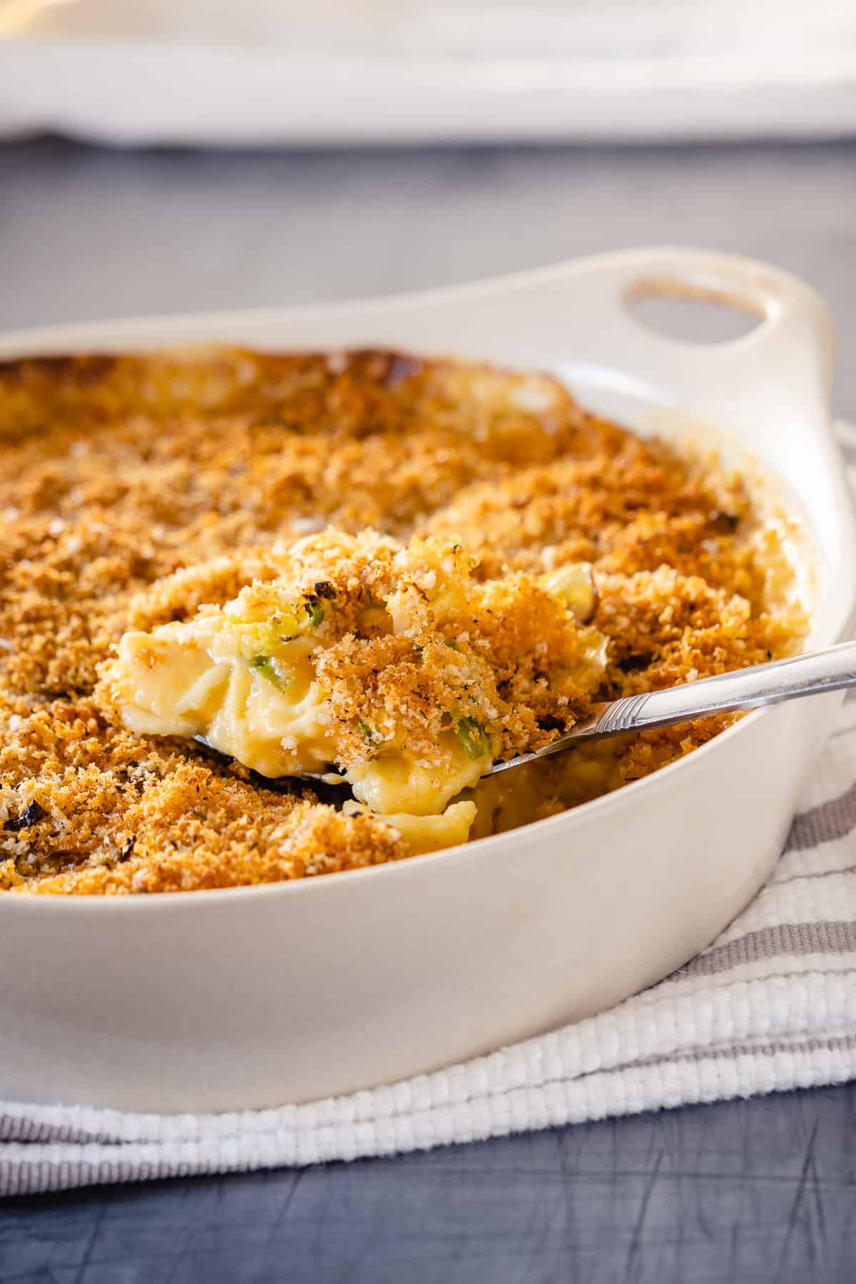 A serving spoon lifting out some Brussels sprouts mac and cheese from a casserole dish