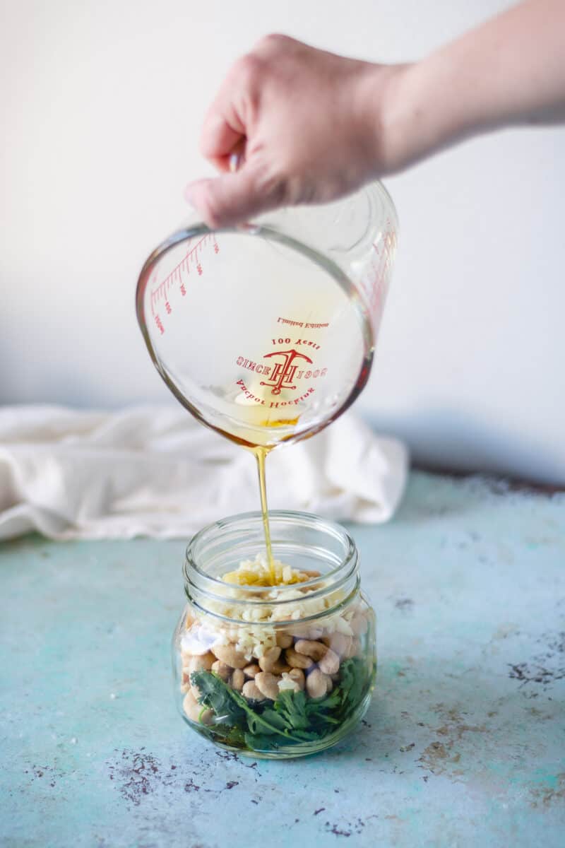 Olive oil being poured into a jar with cashews and cilantro