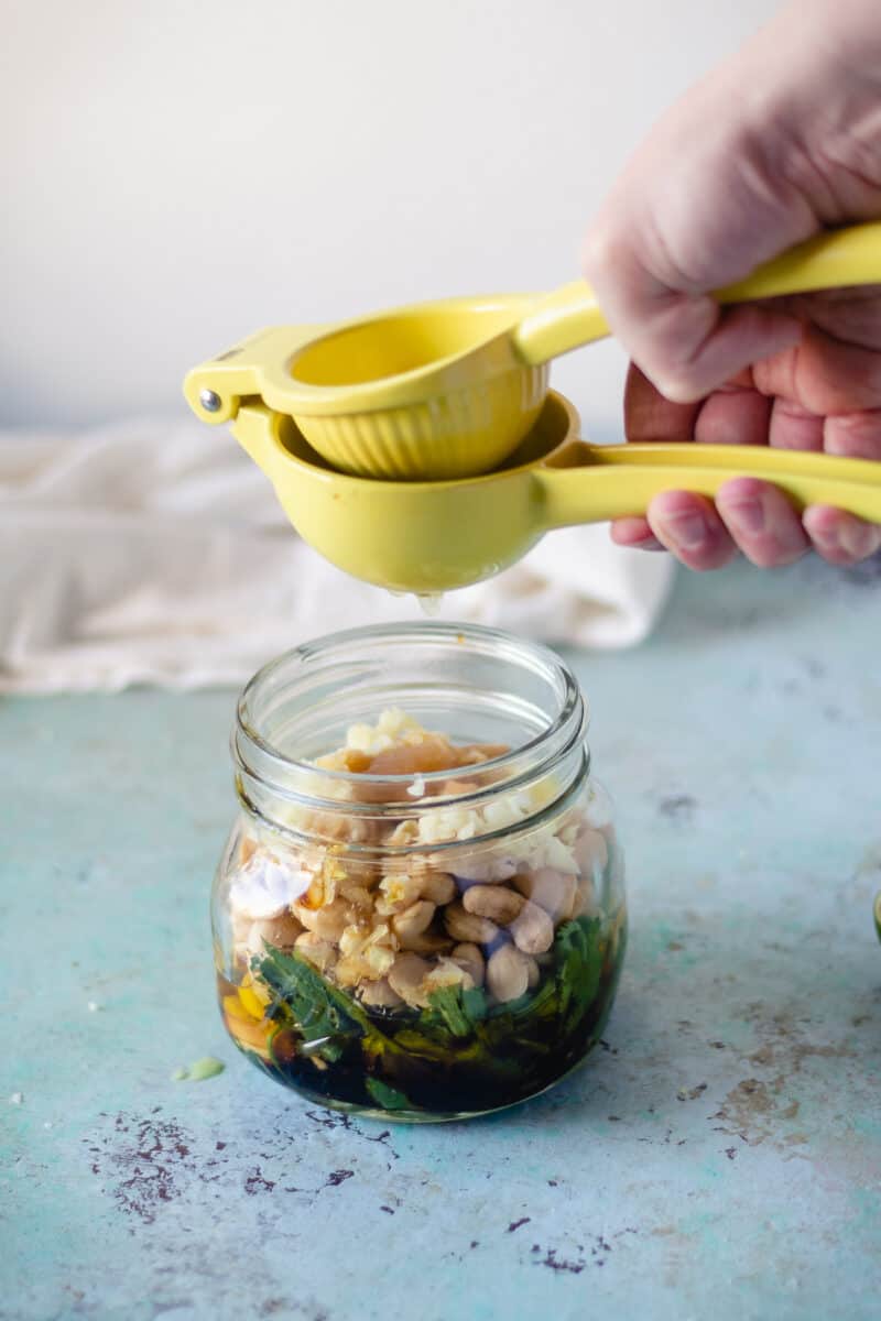 Hand-squeezing lime juice into jar with cashews and garlic and herbs