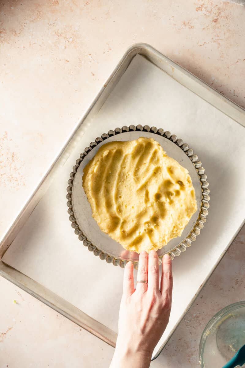 Shortbread tart dough being pressed into a tart pan on a baking sheet