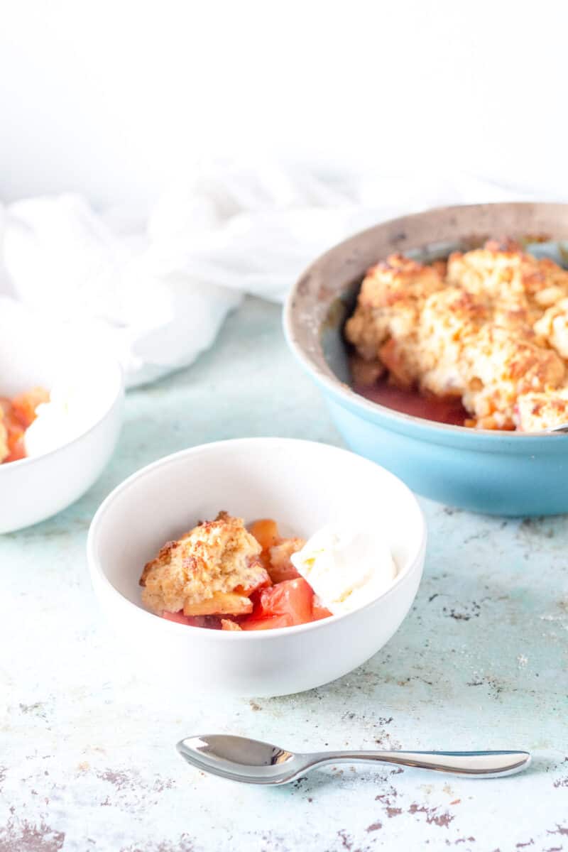 Bowl with peach cobbler and ice cream with baking dish in the background