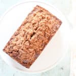 Streusel-topped banana bread with chocolate and pecans on a white cake stand