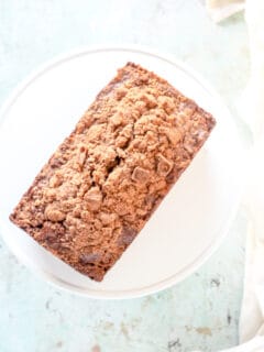 Streusel-topped banana bread with chocolate and pecans on a white cake stand