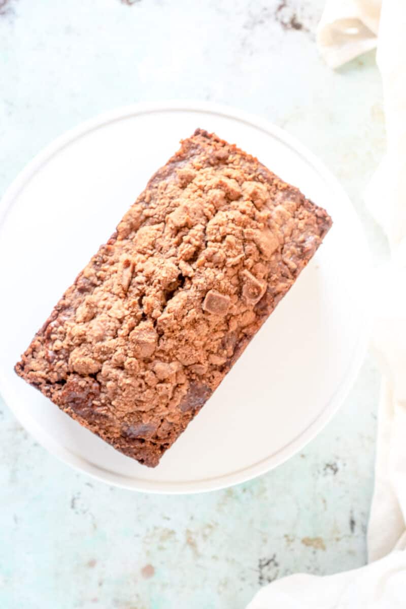 Streusel-topped banana bread with chocolate and pecans on a white cake stand