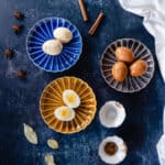 Marbled Chinese tea eggs, two peeled on a plate, three still in the shell, one egg split in half showing the yolk