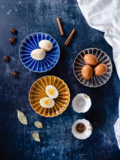 Marbled Chinese tea eggs, two peeled on a plate, three still in the shell, one egg split in half showing the yolk