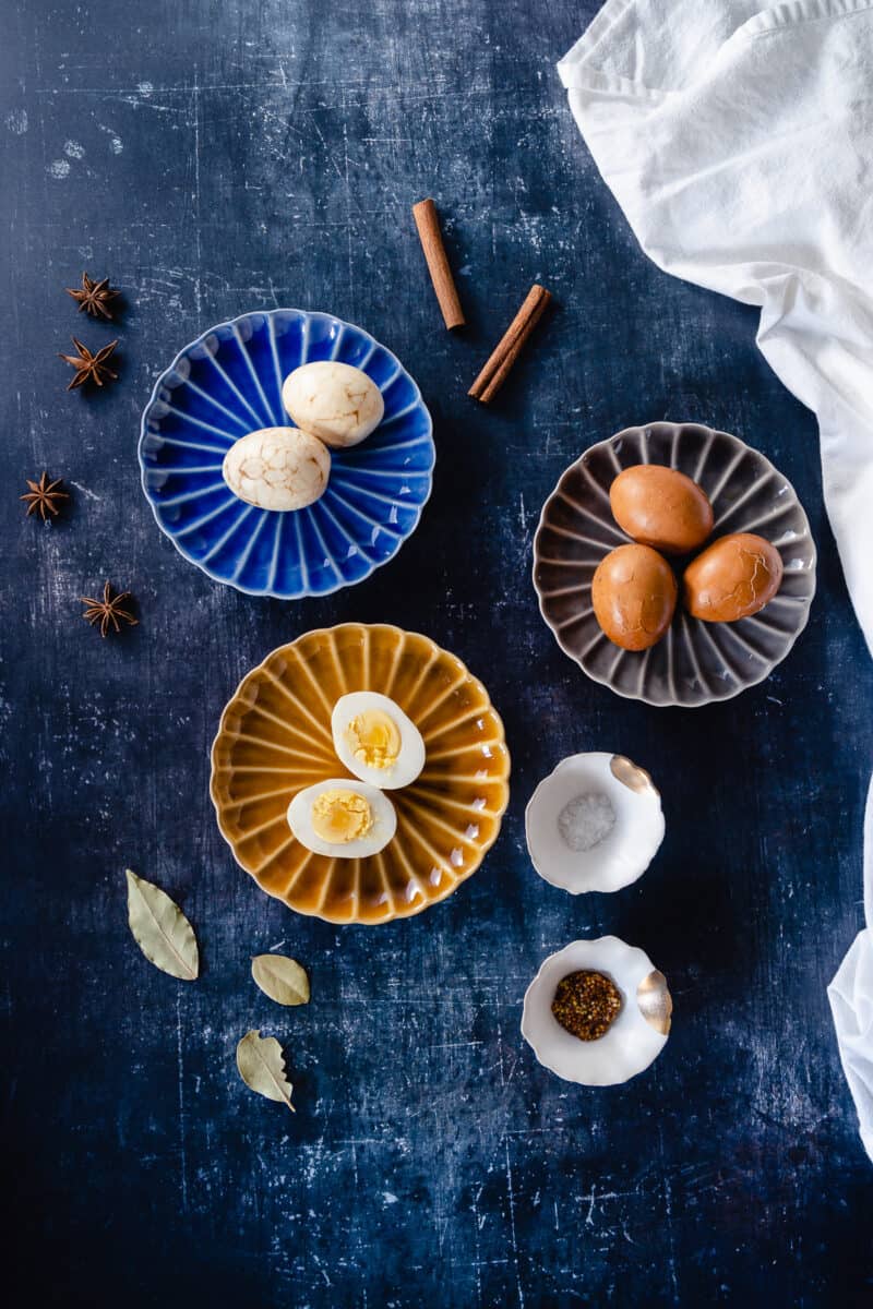 Marbled Chinese tea eggs, two peeled on a plate, three still in the shell, one egg split in half showing the yolk