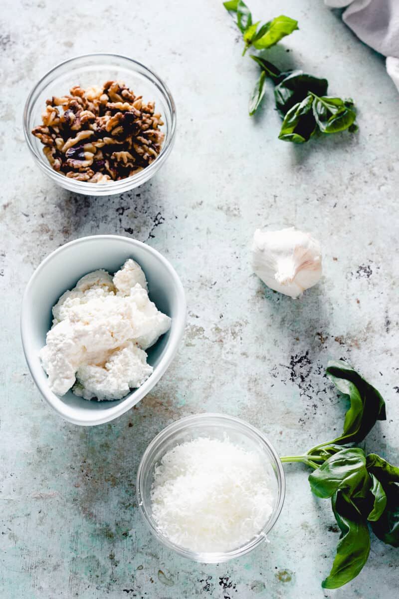 Walnuts, garlic, pecorino romano, and fresh ricotta cheese, and sprigs of basil in bowls